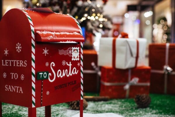Letters to Santa - 11/2/2024 – 12/15/2024 - a Red Mailbox with writing that says Letters to Santa in front of a tree and presents