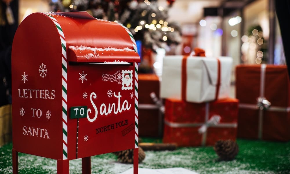 Letters to Santa - 11/2/2024 – 12/15/2024 - a Red Mailbox with writing that says Letters to Santa in front of a tree and presents